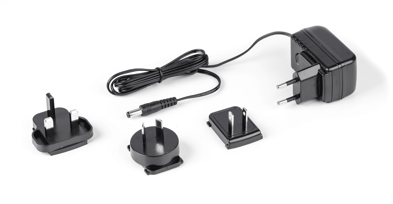 Schwarzes Netzadapter Set auf weißem Hintergrund. Das Set besteht aus einem Stecker mit gefaltetem Kabel und drei Adapter. Die Adapter sind für die Bereiche CH, US und UK.