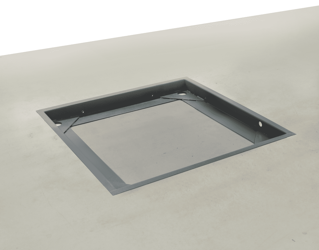 Grubenrahmen aus Stahl in einem grauen Betonboden eingelassen. Die Grube ist offen und ein paar Zentimeter tief. 