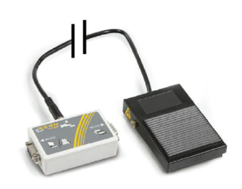 Schwarzer Fußtaster auf weißem Hintergrund. Der Fußtaster ist mit einem Kabel an ein Modul angeschlossen. 